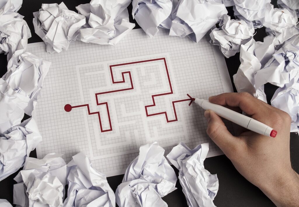 A maze on grid paper with a person drawing their way through it - discarded paper lies around the edges